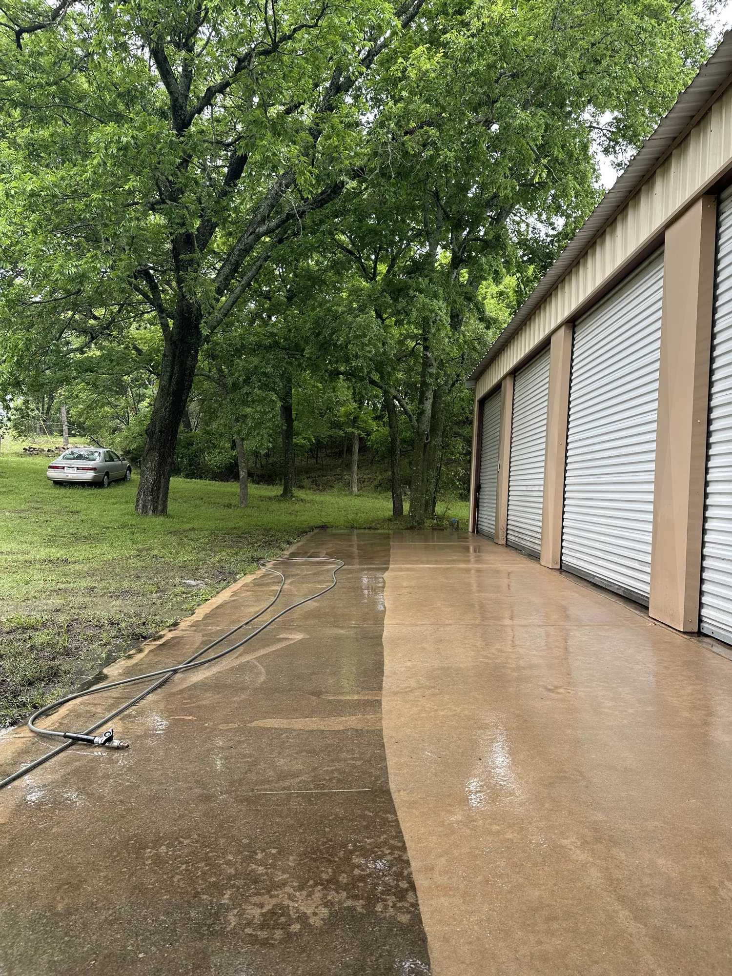 Long concrete apron beside a metal building with white roll-up doors, one wet strip of the concrete lighter than the rest.
